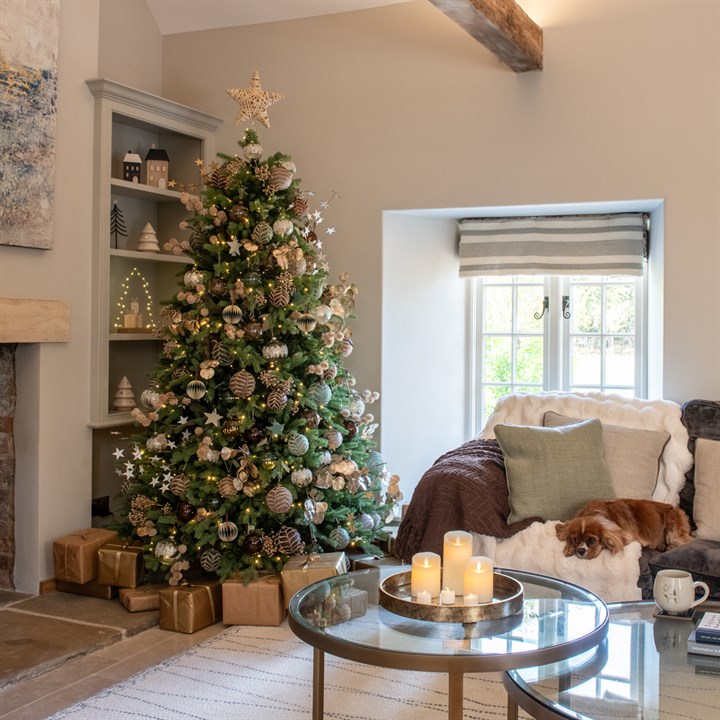 A beautifully decorated tree in a living room, with candles on the table and a dog asleep on the sofa